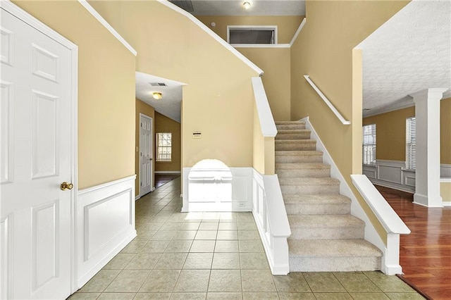 staircase with ornate columns, wainscoting, tile patterned flooring, and a decorative wall