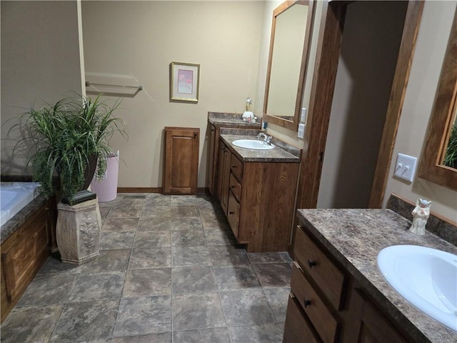 bathroom with baseboards, two vanities, a sink, and a garden tub