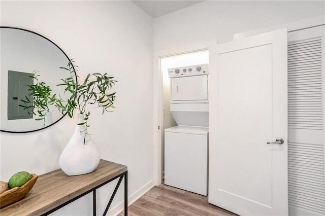 laundry area featuring electric panel, stacked washer / drying machine, and light wood-type flooring