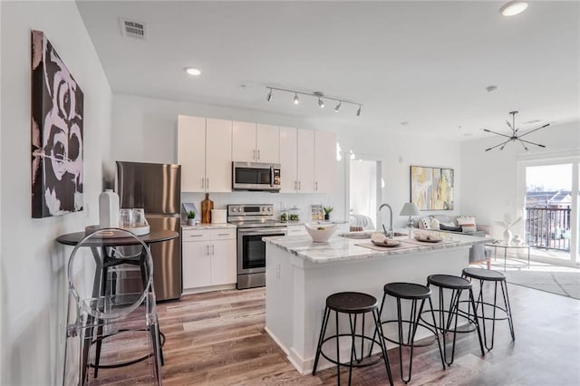 kitchen featuring appliances with stainless steel finishes, white cabinetry, an island with sink, a kitchen breakfast bar, and light hardwood / wood-style flooring