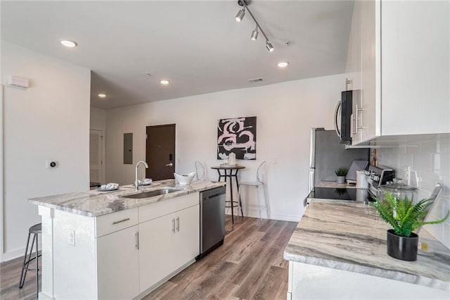 kitchen featuring appliances with stainless steel finishes, sink, white cabinets, light stone countertops, and a center island with sink