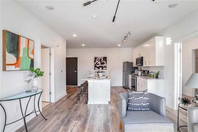 kitchen with light hardwood / wood-style floors, white cabinetry, a breakfast bar, an island with sink, and stainless steel appliances