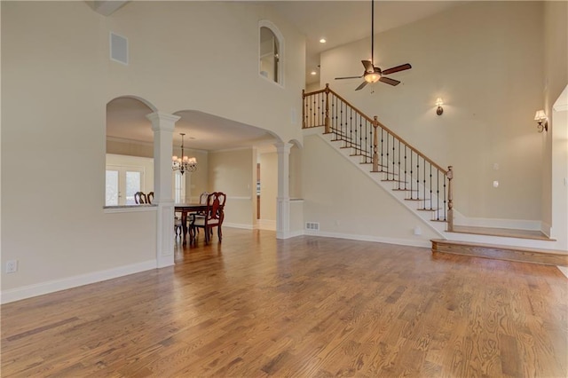 unfurnished living room with wood finished floors, arched walkways, decorative columns, baseboards, and stairs