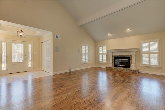 unfurnished living room featuring visible vents, beamed ceiling, a glass covered fireplace, wood finished floors, and baseboards