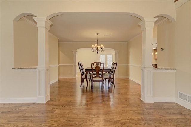 dining space with decorative columns, wood finished floors, visible vents, and ornamental molding