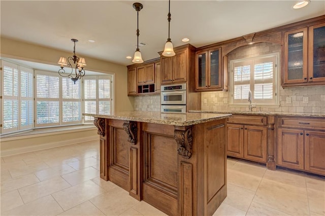 kitchen featuring tasteful backsplash, a center island, light stone countertops, brown cabinets, and a sink