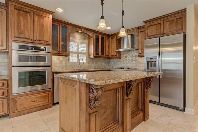 kitchen featuring a sink, light stone counters, stainless steel appliances, brown cabinetry, and wall chimney range hood