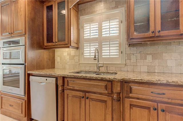 kitchen featuring light stone countertops, dishwashing machine, brown cabinets, stainless steel double oven, and a sink