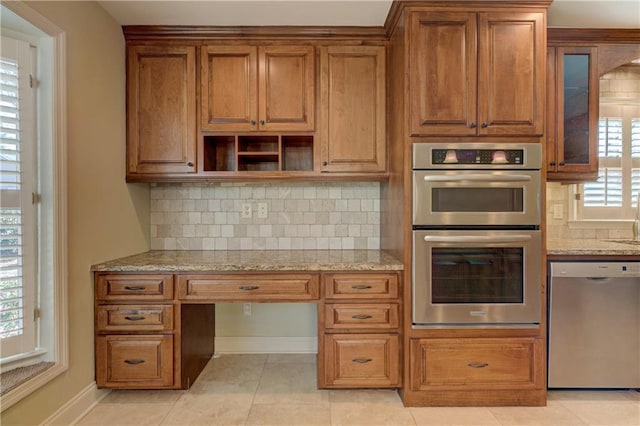 kitchen with brown cabinets, light stone counters, appliances with stainless steel finishes, a healthy amount of sunlight, and built in study area