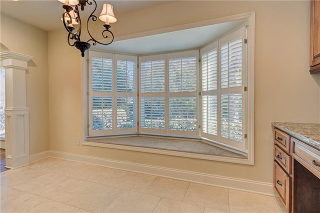 unfurnished dining area with a notable chandelier, decorative columns, baseboards, and light tile patterned floors