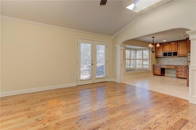 unfurnished living room featuring arched walkways, crown molding, light wood finished floors, decorative columns, and lofted ceiling