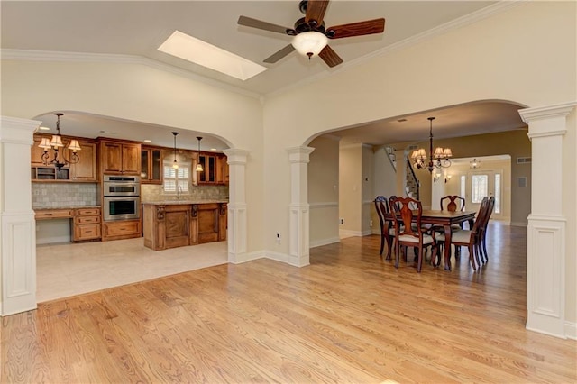 dining room with ceiling fan with notable chandelier, crown molding, light wood-type flooring, and ornate columns