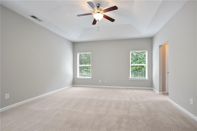 unfurnished room with a tray ceiling, ceiling fan, light carpet, and baseboards
