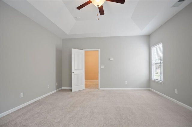 unfurnished bedroom with light carpet, a tray ceiling, a ceiling fan, and baseboards