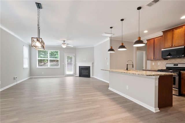 kitchen with gas range, crown molding, a ceiling fan, decorative backsplash, and a glass covered fireplace