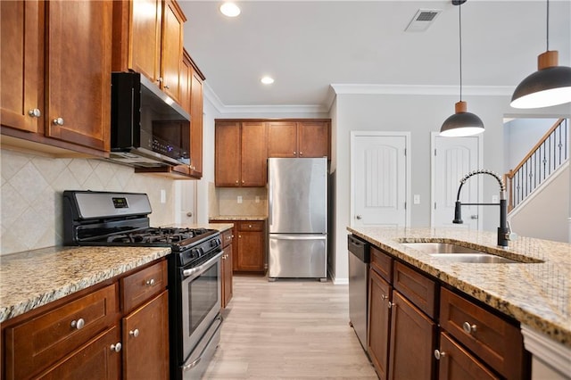 kitchen featuring stainless steel appliances, a sink, ornamental molding, light stone counters, and light wood-type flooring