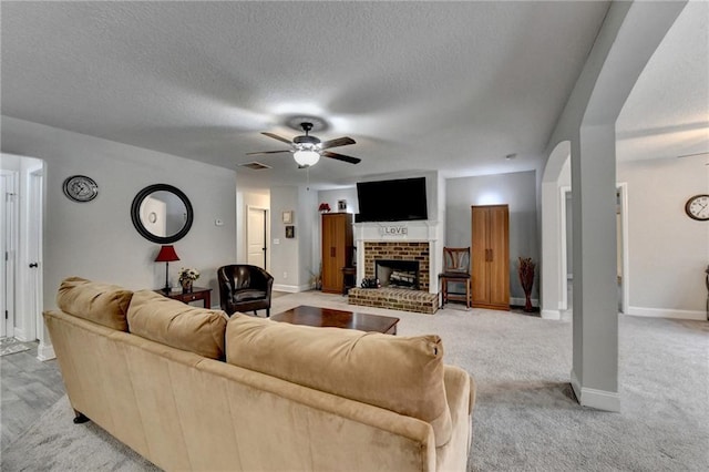 living room with light carpet, a fireplace, ceiling fan, and a textured ceiling