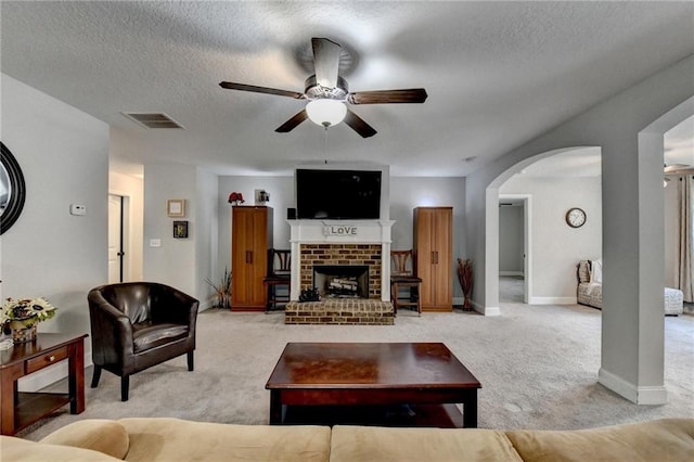 living room with light carpet, a textured ceiling, ceiling fan, and a fireplace