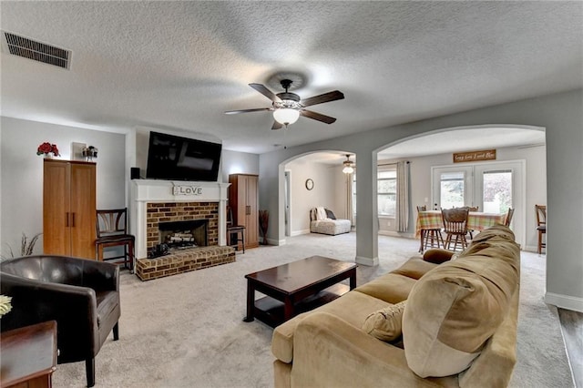 carpeted living room with ceiling fan, a textured ceiling, and a brick fireplace