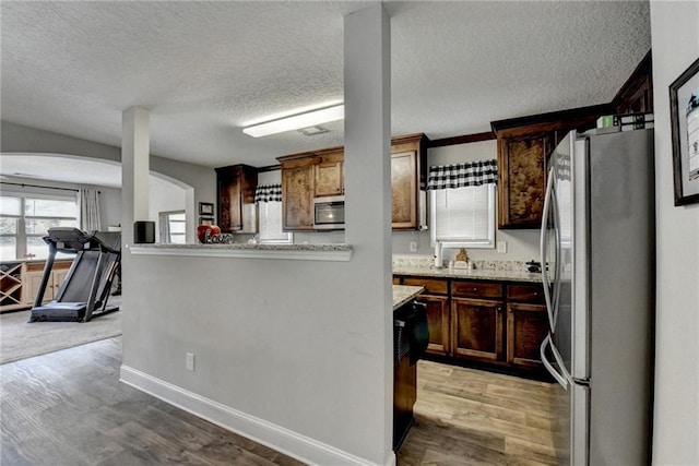 kitchen featuring kitchen peninsula, light stone counters, a textured ceiling, stainless steel appliances, and hardwood / wood-style floors