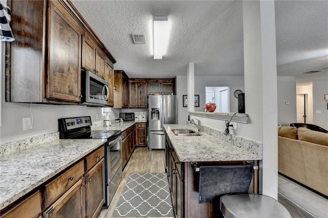 kitchen with dark brown cabinetry, sink, stainless steel appliances, a textured ceiling, and light wood-type flooring