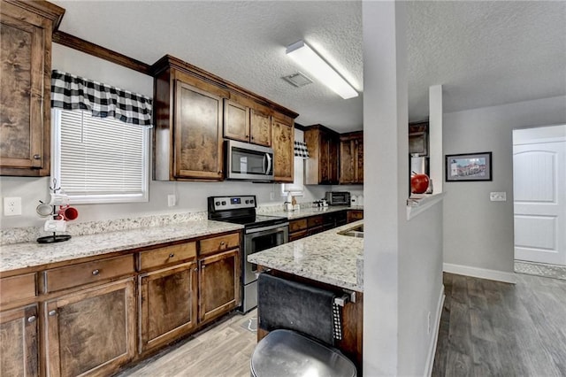 kitchen with light stone counters, stainless steel appliances, a textured ceiling, and light hardwood / wood-style floors