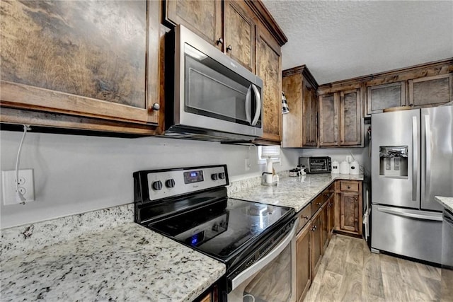 kitchen featuring dark brown cabinetry, light stone counters, a textured ceiling, appliances with stainless steel finishes, and light wood-type flooring