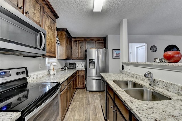 kitchen featuring light stone countertops, sink, light hardwood / wood-style floors, a textured ceiling, and appliances with stainless steel finishes