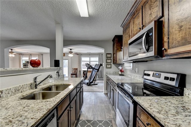 kitchen with sink, light hardwood / wood-style flooring, light stone countertops, a textured ceiling, and appliances with stainless steel finishes