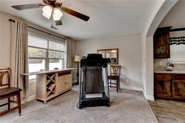 workout room featuring ceiling fan, wood-type flooring, and a textured ceiling