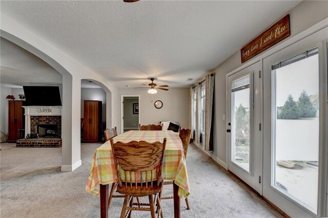 dining room with light carpet, ceiling fan, a textured ceiling, and a brick fireplace