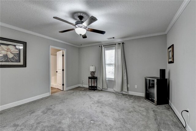 unfurnished room featuring a textured ceiling, light colored carpet, ceiling fan, and ornamental molding