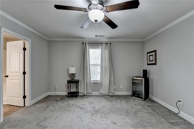 carpeted empty room featuring a textured ceiling, ceiling fan, and crown molding