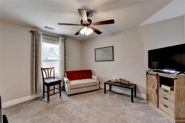 sitting room with ceiling fan, light colored carpet, and a textured ceiling