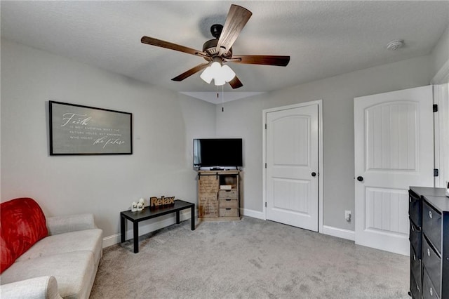 living area with ceiling fan, light colored carpet, and a textured ceiling