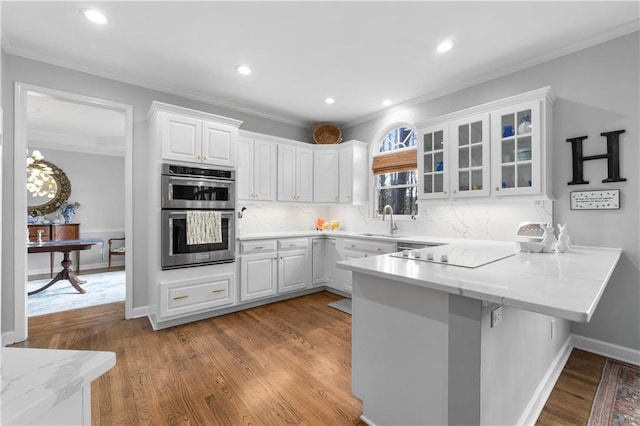 kitchen featuring double oven, electric stovetop, a peninsula, a sink, and white cabinetry