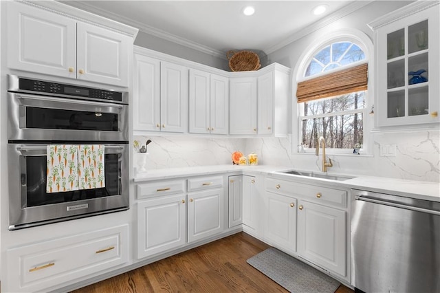 kitchen featuring dark wood finished floors, decorative backsplash, appliances with stainless steel finishes, white cabinetry, and a sink