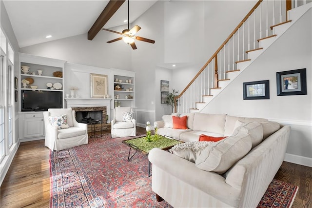 living room featuring a fireplace with raised hearth, wood finished floors, beamed ceiling, baseboards, and stairs