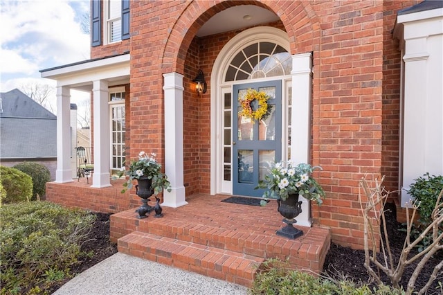 view of exterior entry featuring brick siding and a porch