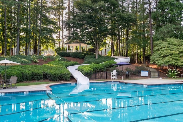 community pool with fence, a water slide, and a patio