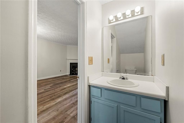 bathroom featuring a fireplace, toilet, a textured ceiling, vanity, and wood finished floors