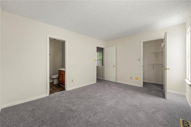 unfurnished bedroom with a textured ceiling, carpet floors, visible vents, baseboards, and a spacious closet