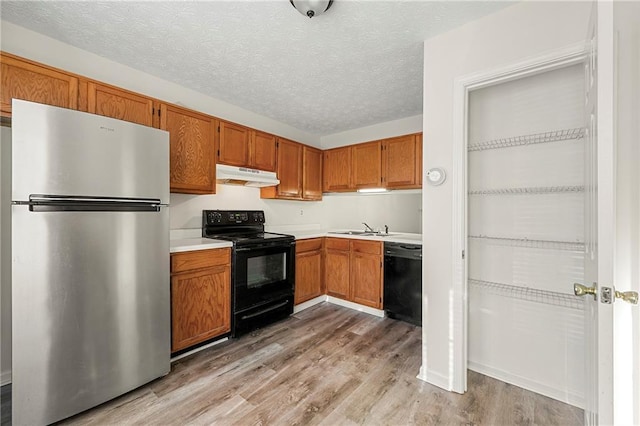 kitchen with light countertops, a sink, light wood-type flooring, under cabinet range hood, and black appliances