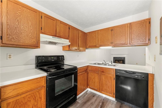 kitchen with under cabinet range hood, a sink, light countertops, black appliances, and dark wood finished floors