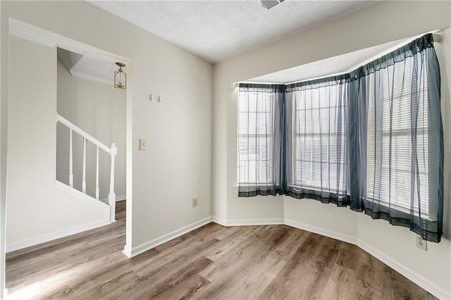 unfurnished room with stairs, a textured ceiling, baseboards, and wood finished floors