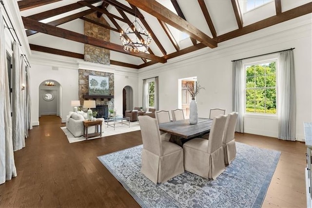 dining space featuring hardwood / wood-style floors, a stone fireplace, a notable chandelier, high vaulted ceiling, and beamed ceiling