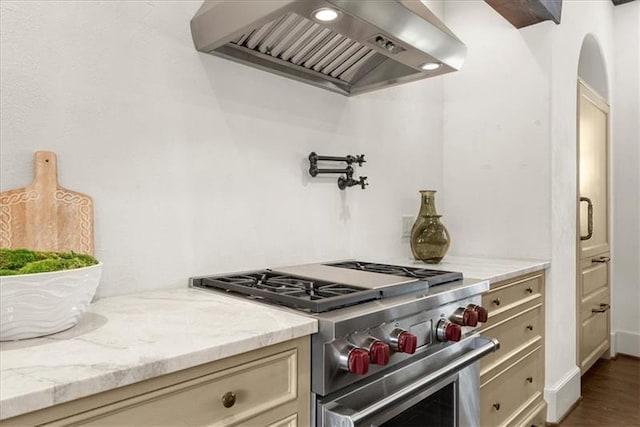 kitchen featuring light stone countertops, wall chimney exhaust hood, hardwood / wood-style flooring, high end stainless steel range oven, and cream cabinetry