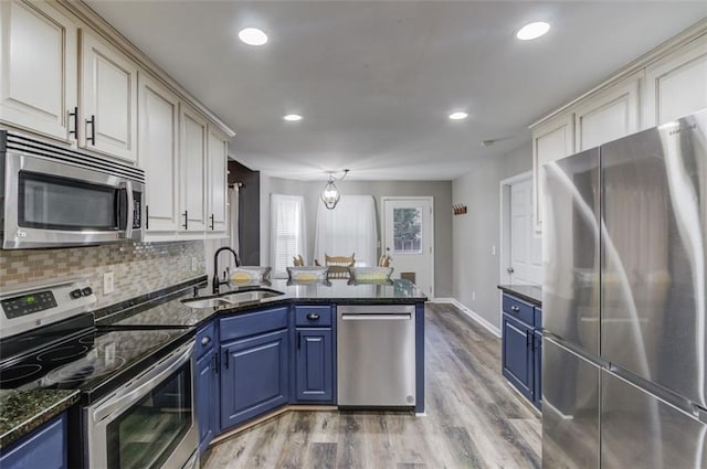 kitchen with appliances with stainless steel finishes, dark stone counters, sink, light hardwood / wood-style flooring, and blue cabinets