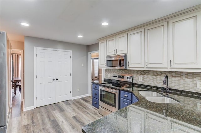 kitchen with appliances with stainless steel finishes, sink, backsplash, blue cabinetry, and dark stone counters