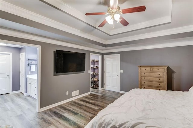 bedroom with ceiling fan, a tray ceiling, ornamental molding, a walk in closet, and connected bathroom